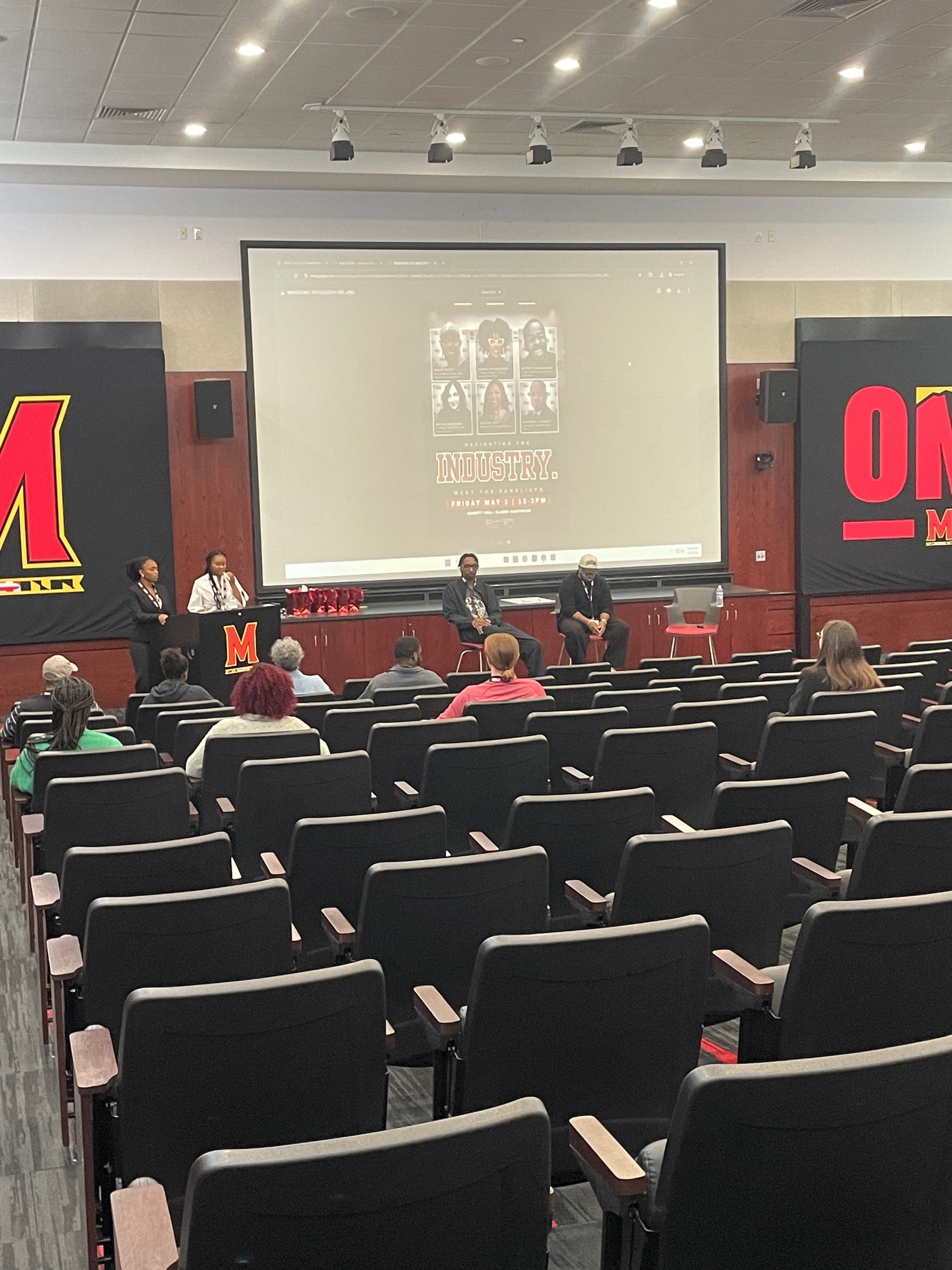 The "Navigating the Industry" career panel underway in a University of Maryland auditorium, with panelist headshots projected on screen.